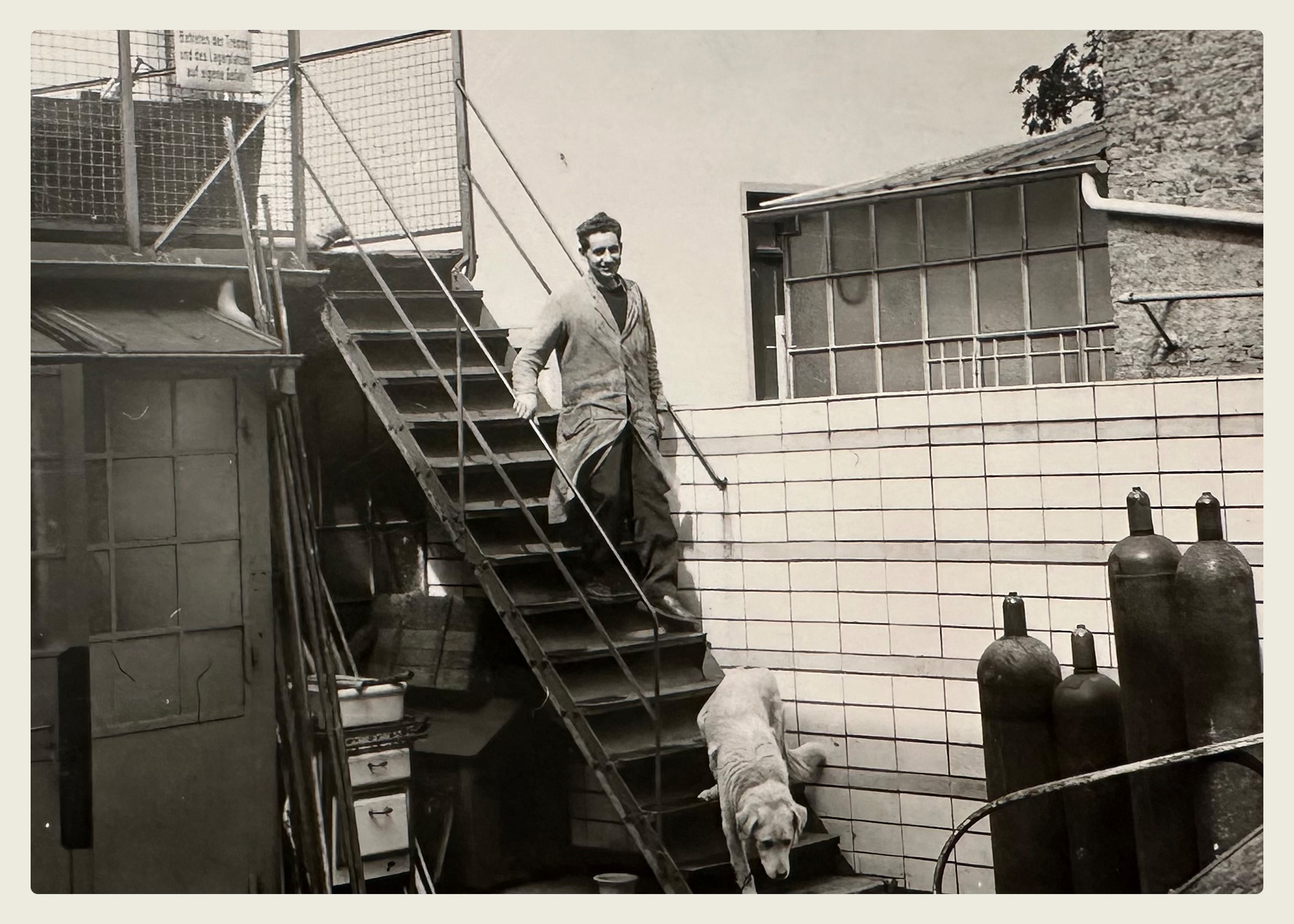 Ein Mann und ein Hund auf einer Treppe im Hinterhof mit Gasflaschen, historische Aufnahme aus dem Archiv